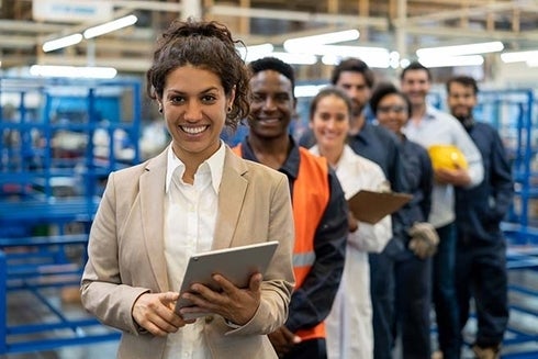 A woman holding a tablet with a group of people behind her. Private Sector - Inter-American Development Bank - IDB