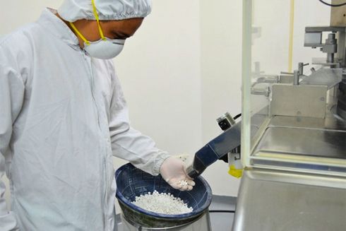 A person in a white robe and mask pouring white granules into a container. Medicine - Inter-American Development Bank - IDB