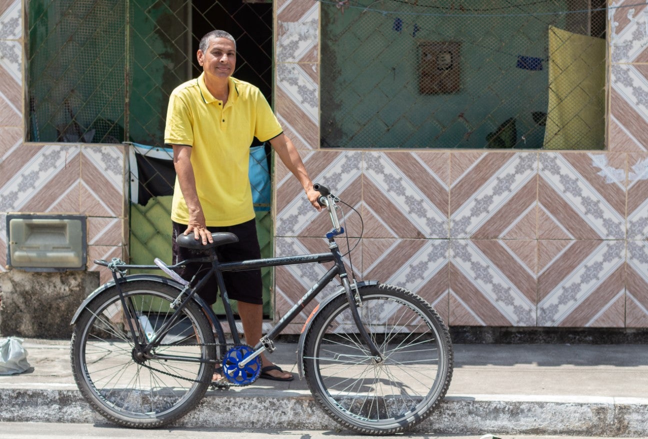 Aldo Lima Santos in front of his house holding his bicycle - Urban Development - Inter-American Development Bank - IDB