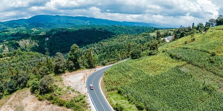 a car driving on a road with a green field and trees Development - Inter-American Development Bank - IDB