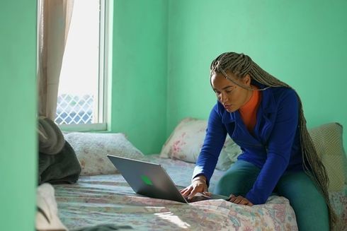 a person sitting on a bed using a laptop work - Inter-American Development Bank - IDB