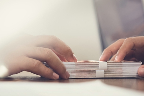 Two hands on a pile of bills or money - Inter American Development Bank - Research at the IDB