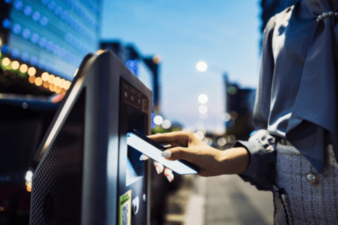 Medium shot of a person with their right hand bringing their mobile phone closer to a digital touchscreen - Inter American Development Bank - IDB Impact