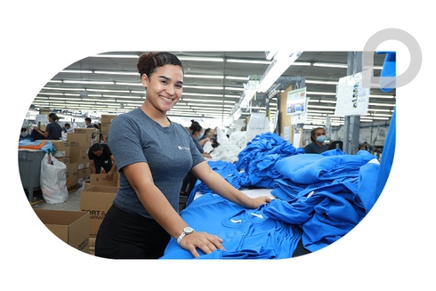 Woman with her arms held up by garments in a factory - Inter American Development Bank - Institutional Strategy